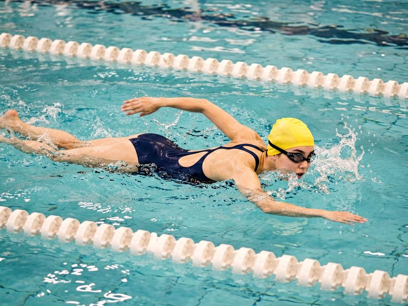 Four burst frames of a swimmer in a yellow cap, mid-stroke.